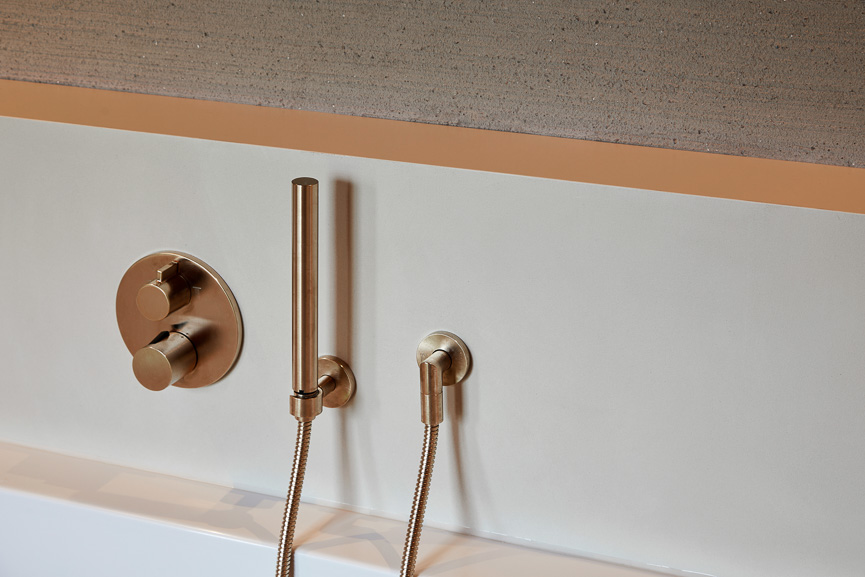 Detail Wandarmatur in Roségold mit Handbrause an fugenloser Wand aus mineralischem Erdton